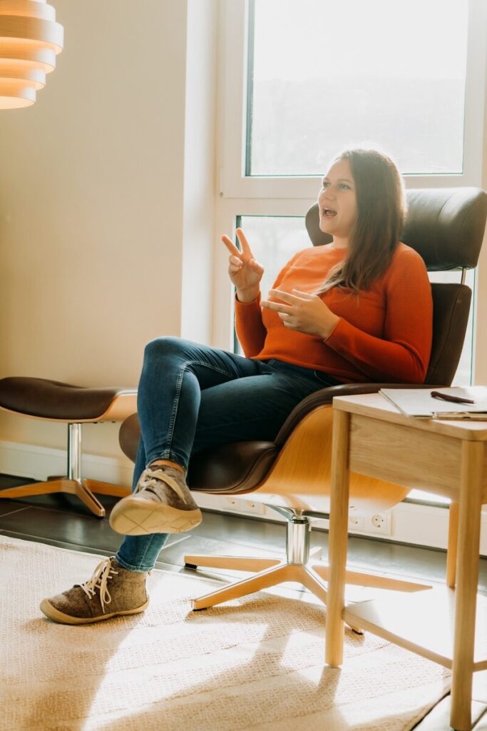 Dana Kaspar in einem schönen Stuhl vor einem Fenster gestikuliert